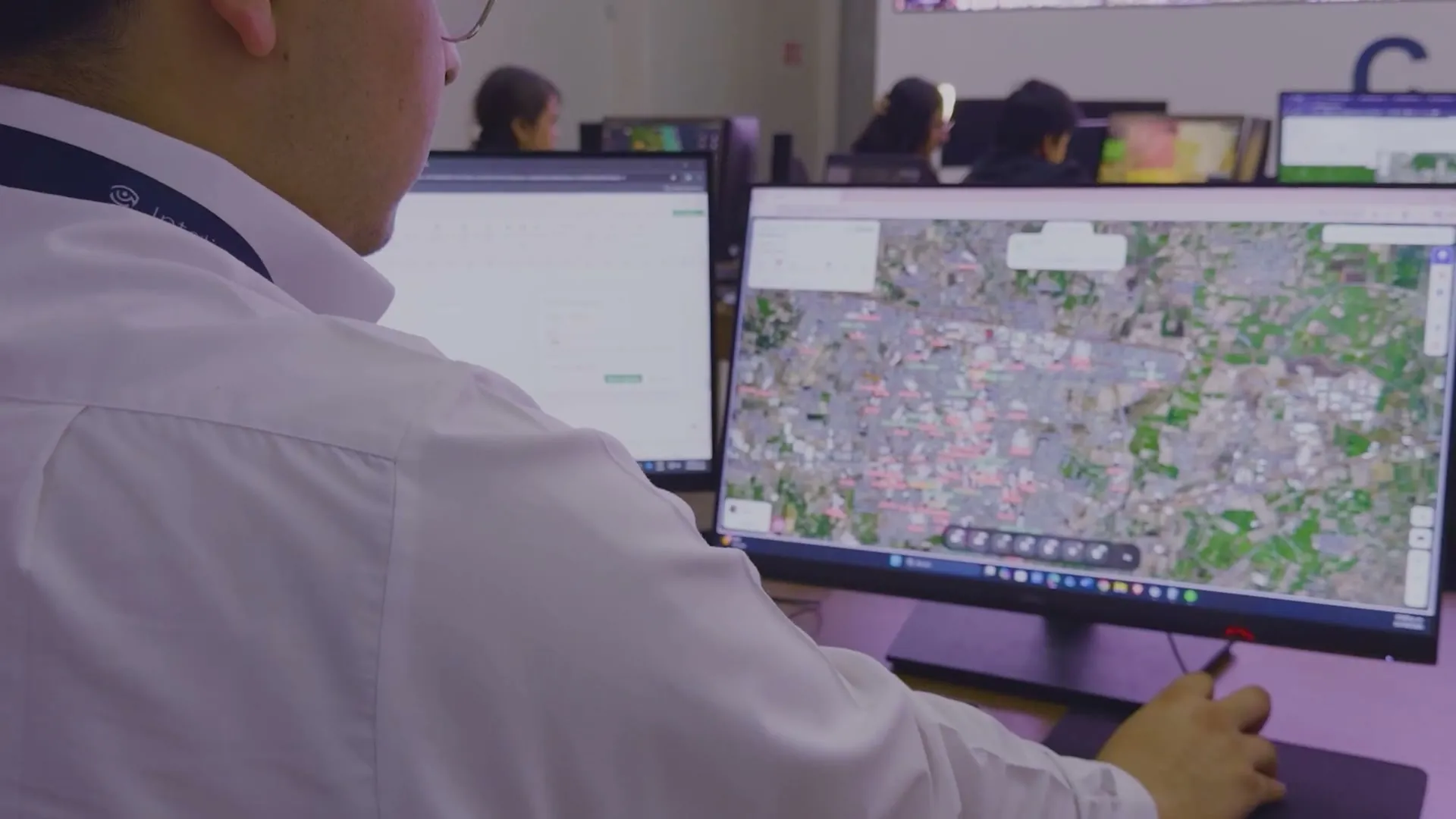 An operator at his monitors in the monitoring center, with colleagues working in the background.